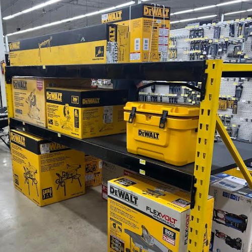 A two-tiered shelf displaying various DeWALT products, including a table saw and a toolbox. A box containing another table saw is placed on the floor below he shelf.