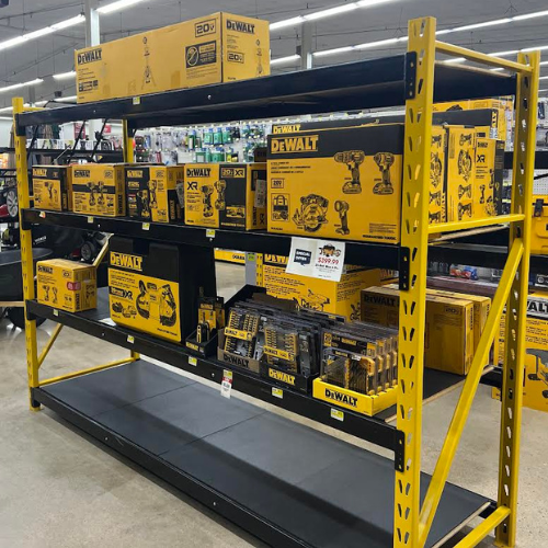 A three-tiered shelf showcasing various DeWALT products, including tool sets with circular saws and drills, drill sets, a work light, drill bits, and other tools.